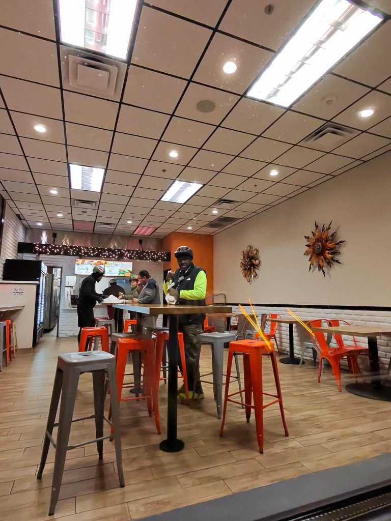 Entrance of Taco Verde restaurant with a neon 'OPEN' sign and catering menu display.