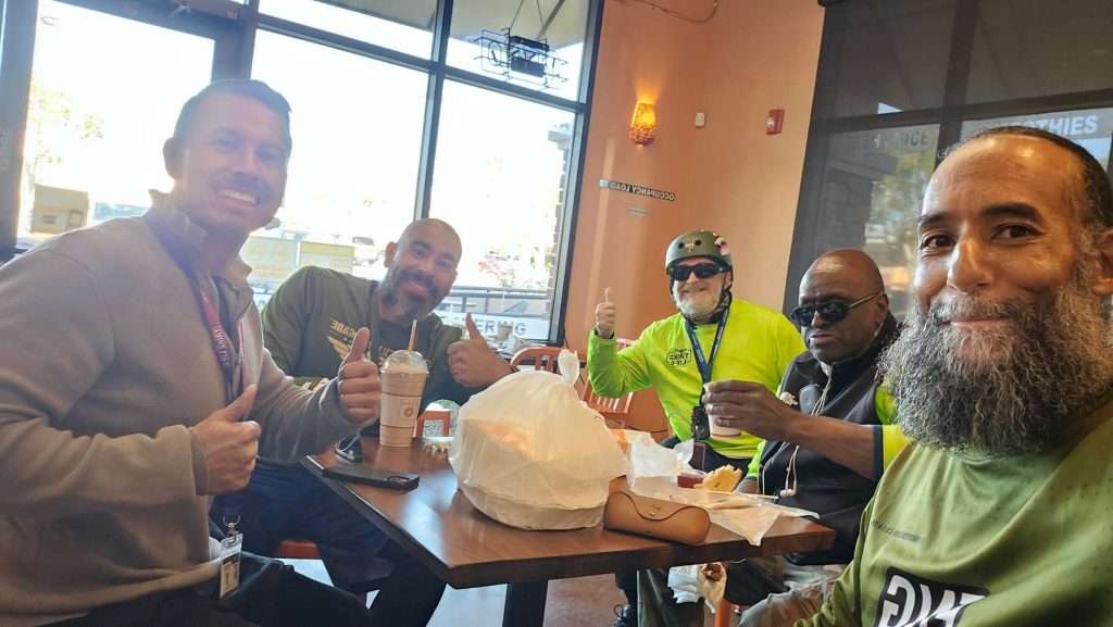 Five veterans seated at a table enjoying refreshments after a Forgotten Not Gone event. Smiles and thumbs-up gestures reflect camaraderie and positivity.